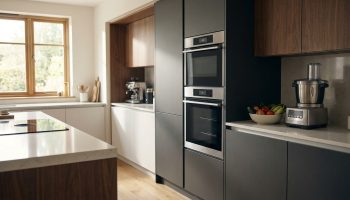 Cuisine moderne et lumineuse équipée d'un double four encastré, plaque à induction, robot culinaire et machine à café, aux tons bois et gris.