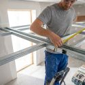 Artisan mesurant une structure métallique pour un plafond autoportant avec un mètre ruban.