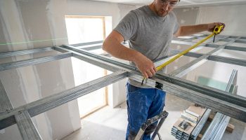 Artisan mesurant une structure métallique pour un plafond autoportant avec un mètre ruban.