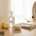 Une personne nettoie une table en bois. Au premier plan, citrons, vaporisateur de nettoyage naturel, poudre blanche et chiffon.