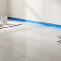 Pièce en rénovation avec murs peints, ruban de masquage bleu, rouleau à peinture et carrelage clair au sol avec outils.