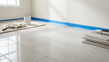 Pièce en rénovation avec murs peints, ruban de masquage bleu, rouleau à peinture et carrelage clair au sol avec outils.