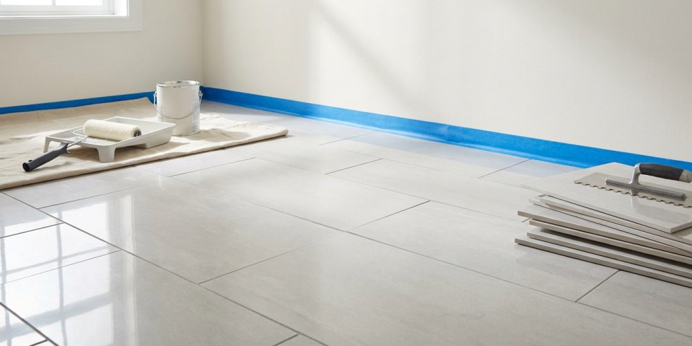 Pièce en rénovation avec murs peints, ruban de masquage bleu, rouleau à peinture et carrelage clair au sol avec outils.