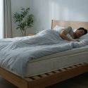 Un homme dort paisiblement dans un lit doté d'un sommier à lattes en bois dans une chambre lumineuse.