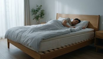 Un homme dort paisiblement dans un lit doté d'un sommier à lattes en bois dans une chambre lumineuse.
